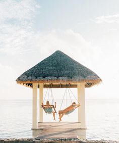 two people laying in hammock chairs on the beach next to an over water gazebo