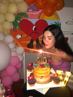 a woman sitting in front of a cake with lit candles on it and surrounded by balloons