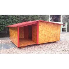 a small wooden dog house sitting on top of a gravel ground next to a bush