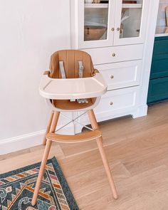 a baby high chair sitting on top of a hard wood floor next to a cabinet