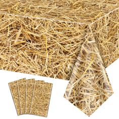 a table covered in hay next to four pieces of paper that have been cut into squares