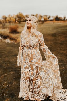 a woman in a long dress standing on the grass with her arms out and looking off into the distance