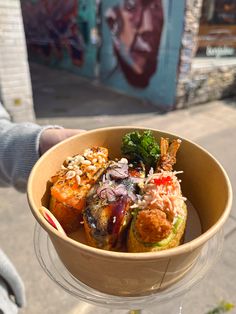 a person holding up a bowl filled with food on top of a street side walk