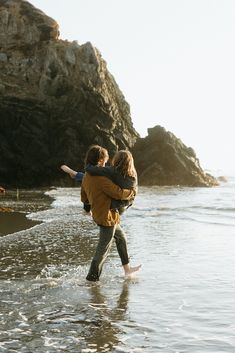 two people are walking along the beach with their arms around each other as they hug