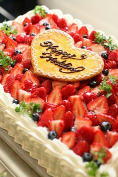 a heart shaped cake with strawberries and blueberries on the bottom is decorated with a happy birthday message