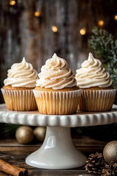 three frosted cupcakes on a cake plate with cinnamon sticks and christmas decorations