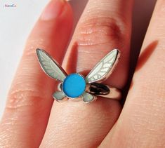 This is a detailed Navi ring inspired by the Legend of Zelda series. These are crafted from solid brass, and then filled with translucent enamels. It would be a perfect gift for any Zelda fan. The width of the ring band comes in two size options, a thicker 4mm version and a thinner 3mm version. Navi Size: 20mm x 12mm Band Material: Brass, Silver Finish Band Thickness: 3mm or 4mm Details: Adjustable Band Size, Tilted Navi Wings, Translucent Enamel This ring band is adjustable to fit, and the defa Zelda Clothes, Navi Zelda, Zelda Accessories, Zelda Rings, Zelda Navi, Navi Zelda Earrings, Zelda Jewelry, Zelda Merch, Zelda Ring