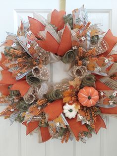 an orange and white wreath with pumpkins, leaves and ribbons on the front door