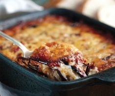 a casserole dish with meat and cheese being spooned into the casserole