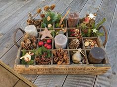 a wooden crate filled with pine cones, candles and other christmas decorations on a deck