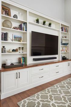 a large flat screen tv sitting on top of a white bookcase in a living room