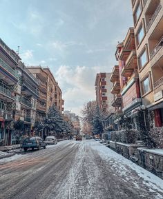 a snowy street with cars parked on the side and buildings in the backgroud