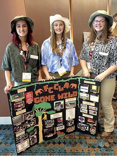 three women standing next to each other holding up a sign with information about plants and animals on it