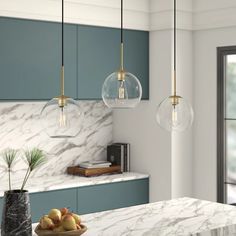 a kitchen with marble counter tops and hanging lights over the island area, along with two vases filled with fruit