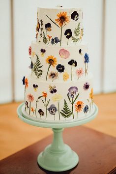 a multi - tiered cake decorated with colorful flowers on a green plate sitting on a wooden table