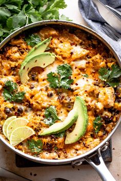 a skillet filled with chicken and rice topped with cilantro, avocado and lime wedges