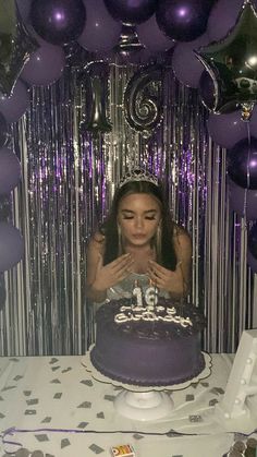 a woman sitting in front of a purple cake surrounded by balloons and confetti