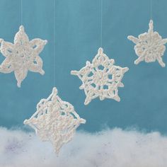 three snowflakes hanging from strings on a blue background with white fluffy clouds in the foreground