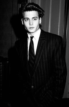 a young man in a suit and tie posing for a black and white photo with his hands in his pockets