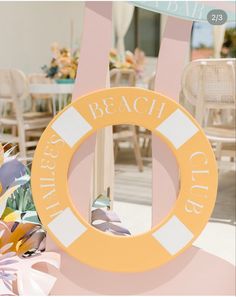 a pink and yellow sign sitting on top of a white table next to flowers in vases