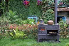 an outdoor wood burning stove in the middle of some flowers and greenery with potted plants