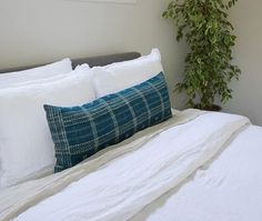 a bed with white linens and pillows on top of it next to a potted plant