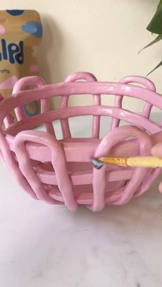 a pink basket that is sitting on a table next to a plant with a pencil in it