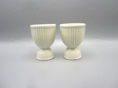 two white vases sitting next to each other on a gray surface with no one around them