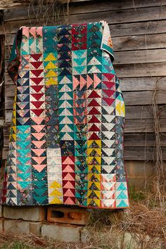 a multicolored quilt hanging on the side of a wooden building next to grass