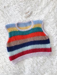 a multicolored knitted sweater hanging on a white furnishing with a chain