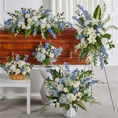 blue and white flowers are arranged in front of a wooden casket with greenery on the side