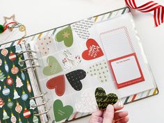 a hand holding a heart shaped paper in front of a christmas themed page book with holiday decorations on it