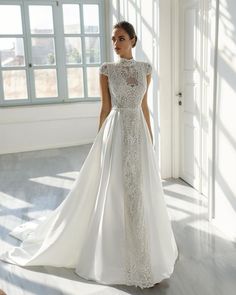 a woman in a white wedding dress standing next to a window and looking off into the distance