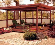 a covered patio area with chairs and flowers in the foreground, surrounded by trees