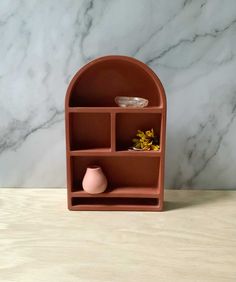 an orange shelf with two vases and a bowl on it in front of a marble wall