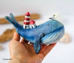 a hand holding a blue whale figurine with a lighthouse on it's back