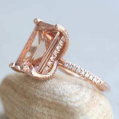 This Diamond Prong Morganite Ring is part of our Olivia Collection, which is characterized by a gorgeous, genuine gemstone with Golden Hearts under it. Diamonds stud the hidden halo and sparkle down the half eternity shank.  Custom initials at the back of the shank are available on all rings upon request!

Center Stone: Genuine AAA Peachy Pink Morganite, Emerald Cut, averaging 15x12mm and 10 carats.
Side Stones: 68 Diamonds – you choose Lab Grown or Organic – averaging F-G, VS2-SI1 and 0.46 cara Radiant Cut Diamond Ring With Gemstone, Radiant Cut Morganite Wedding Jewelry, Radiant Cut Gemstone Halo Ring, Wedding Rings With Radiant Cut Gemstone, Cushion Cut Diamond Ring With Gemstone, Cushion Cut Diamond Gemstone Ring, Luxury Morganite Ring With Prong Setting, Morganite Halo Design Jewelry For Formal Occasions, Dazzling Diamond Halo Ring With Accent Stones