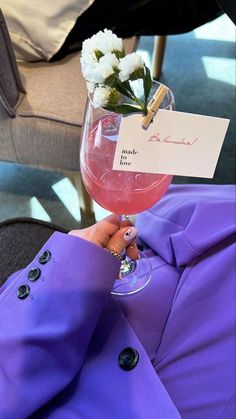 a woman holding a wine glass filled with pink liquid and white flowers on top of it