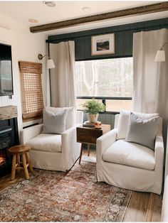 a living room with two white chairs and a rug in front of the fireplace area