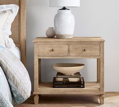 a white vase sitting on top of a table next to a bed