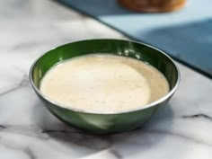 a green bowl filled with cream sitting on top of a marble counter next to doughnuts