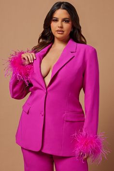 a woman in a bright pink suit with feathers on her lapel and pants, posing for the camera