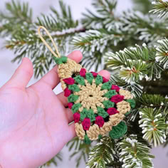 a hand holding a crocheted ornament in front of a pine tree