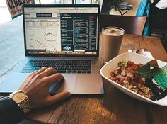 a person sitting in front of a laptop computer on top of a wooden table next to a bowl of food