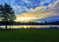 the sun is setting over a lake and lawn chairs are set up on the grass