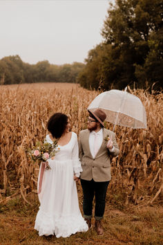 a man and woman holding an umbrella walking through a corn field