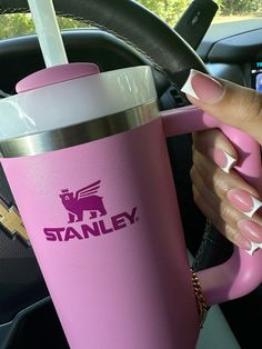 a woman's hand holding a pink coffee cup in her car with the word stanley on it