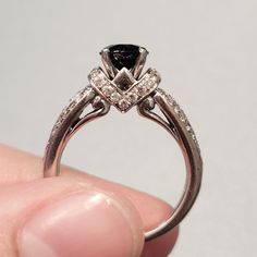 a close up of a person's hand holding a ring with a black diamond