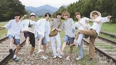 a group of young men standing next to each other on top of train tracks with trees in the background