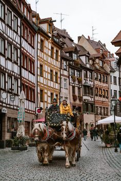 two horses pulling a carriage down a cobblestone street in an old european town